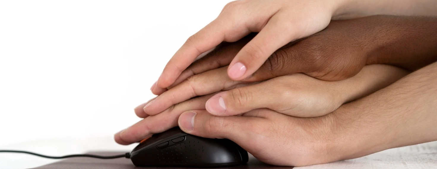 Manos de diferentes personas unidas sobre un ratón de computador, ilustrando la importancia de la accesibilidad digital universal