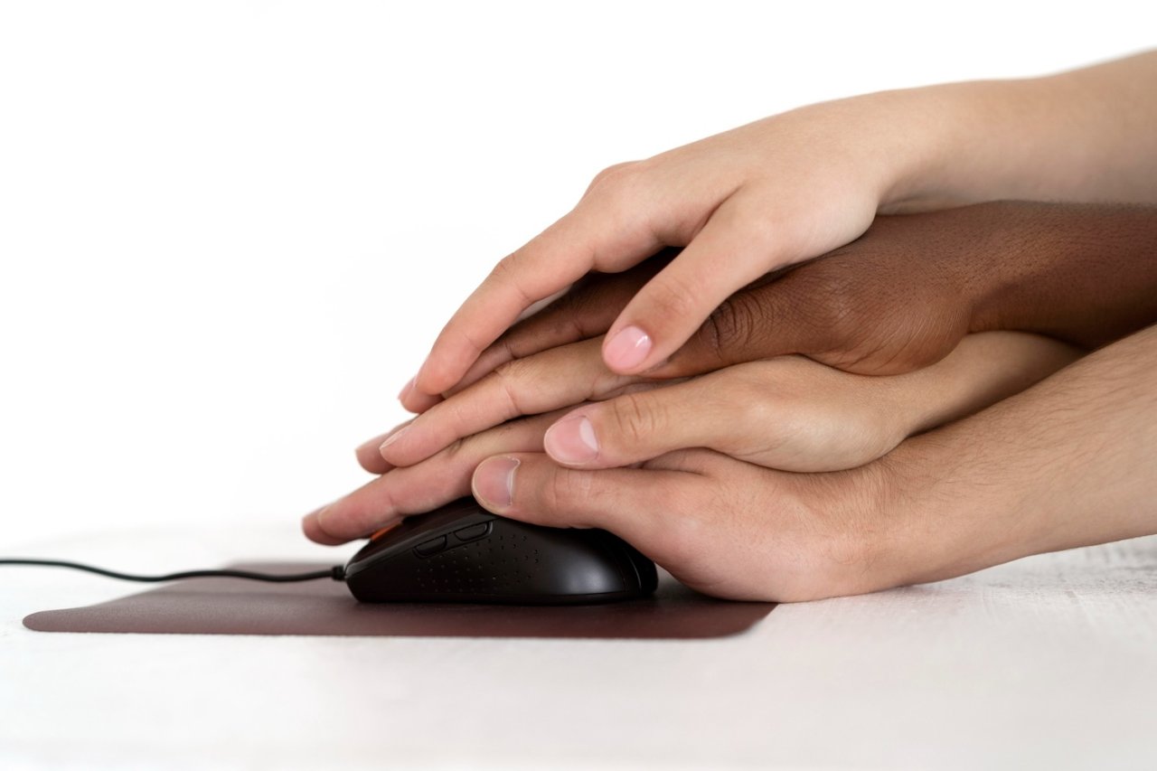 Manos de diferentes personas unidas sobre un ratón de computador, ilustrando la importancia de la accesibilidad digital universal.